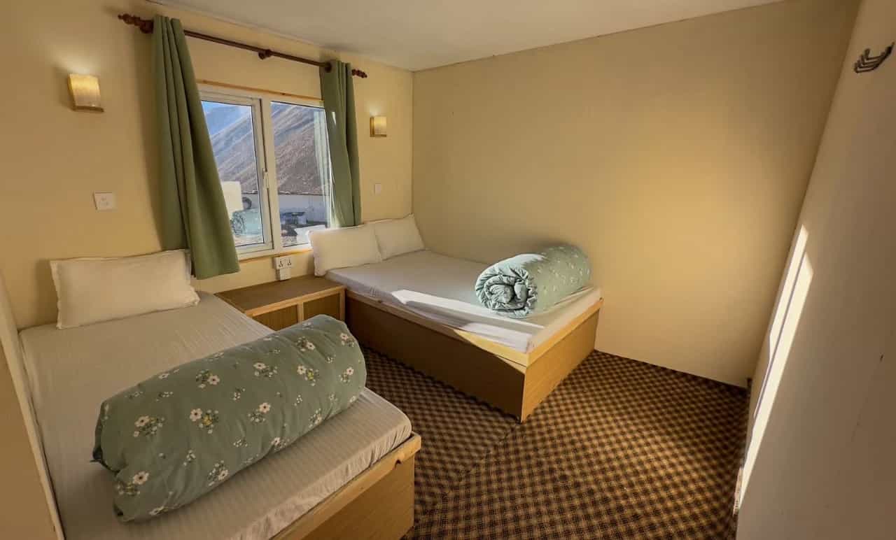 Twin room in Hotel Dingboche with mountain view through window and floral rolled duvets.
