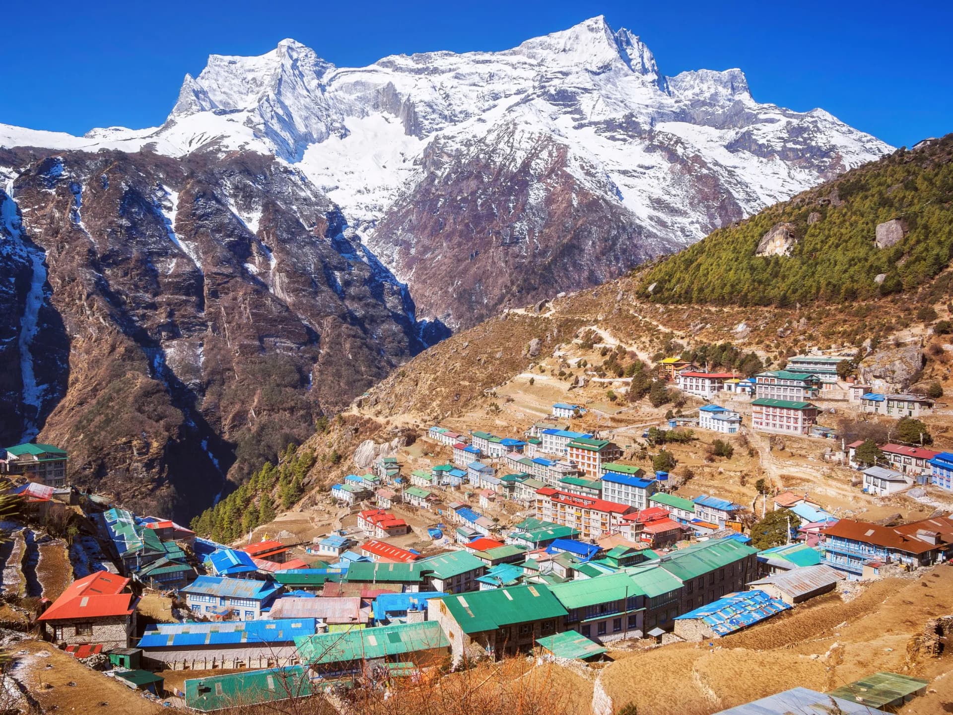Village of Namche Bazaar nestled on a hillside below massive snow-covered Himalayan peaks.