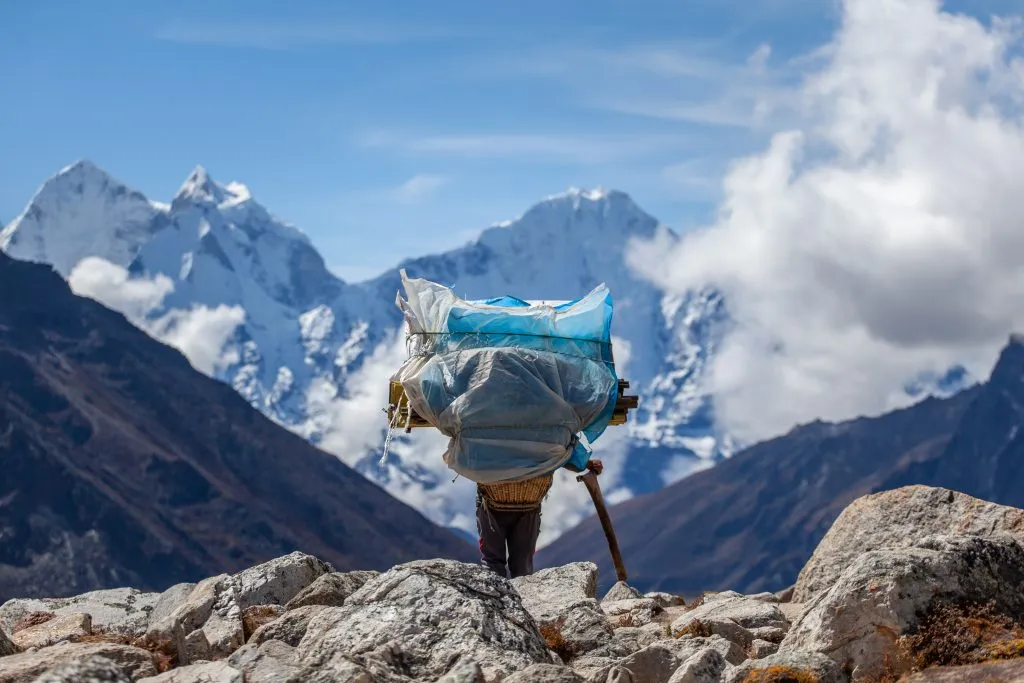 Een drager draagt een zware last op de everest base camp trekking, himalaya, Nepal